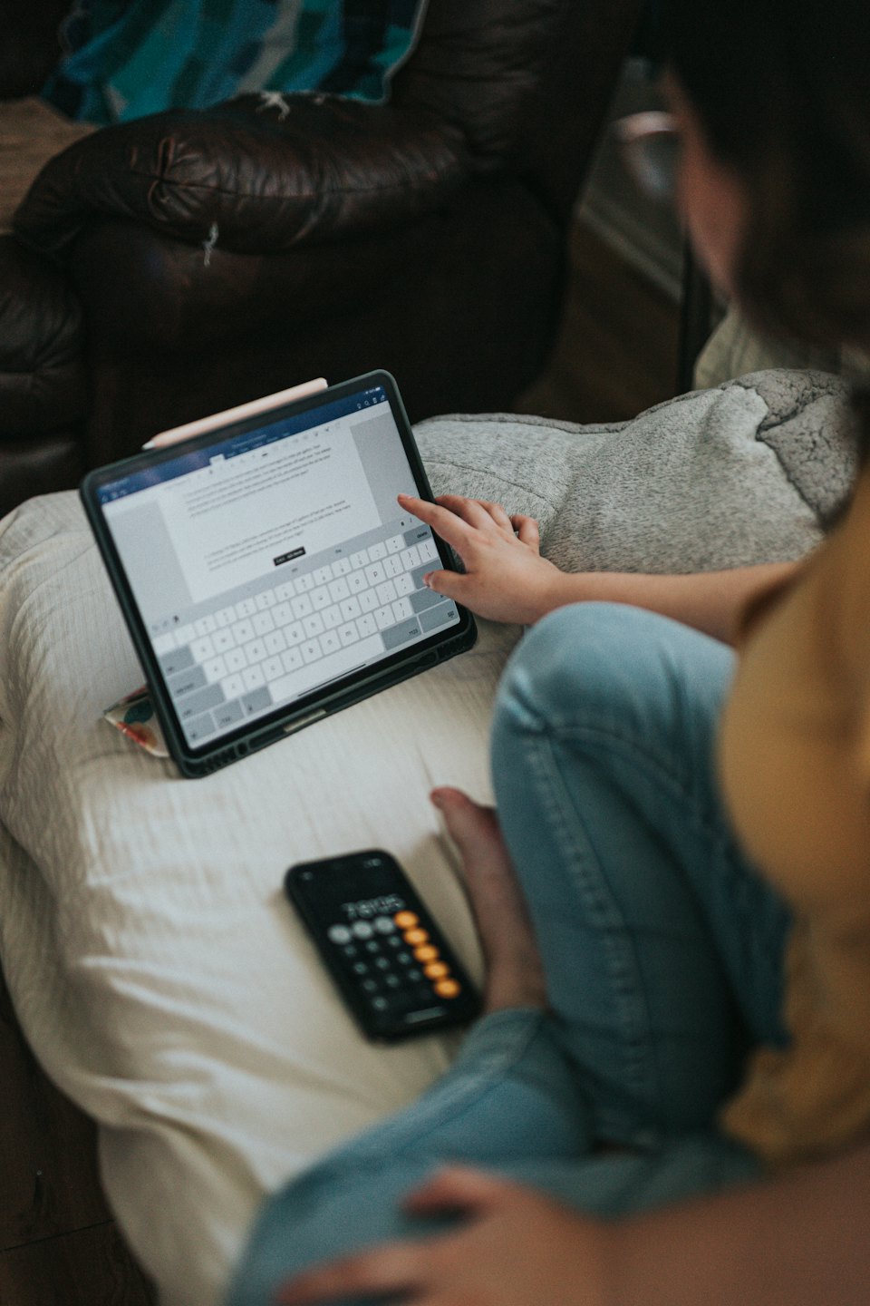 Person typing on a tablet on their lap next to a smartphone.