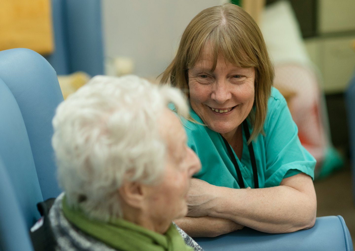 Healthcare worker talking to an elderly person in a care facility.